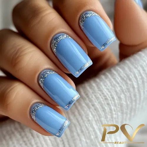 unhas-decorada-azul-quadrada-glitter-maravilhoso-pv-beauty-14 Unhas pintadas de azul claro com bordas prateadas brilhantes, segurando tecido branco.