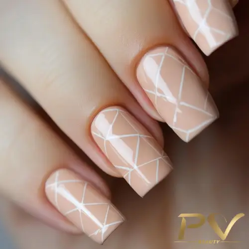 Unhas decoradas com esmalte nude e linhas brancas formando um padrão geométrico.