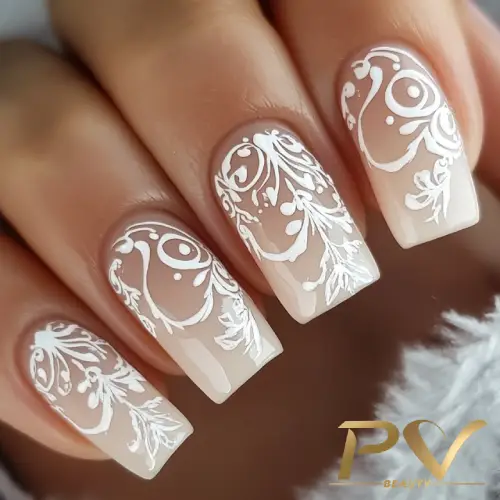 Unhas decoradas com esmalte nude e desenhos brancos delicados em estilo floral.