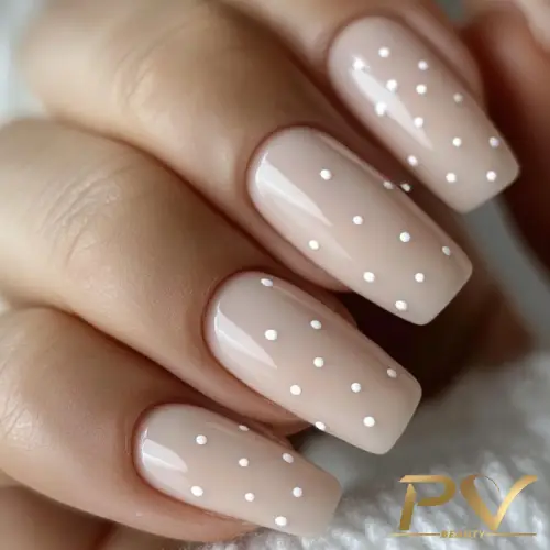 Unhas com esmalte nude e pequenas bolinhas brancas decorativas.