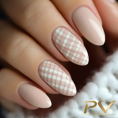 Unhas com esmalte nude e duas decoradas com padrão xadrez em tons claros.