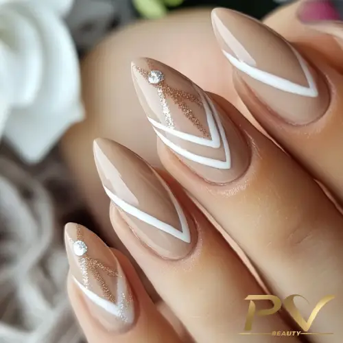Unhas decoradas com esmalte nude, linhas brancas e detalhes brilhantes, incluindo pequenas pedras.