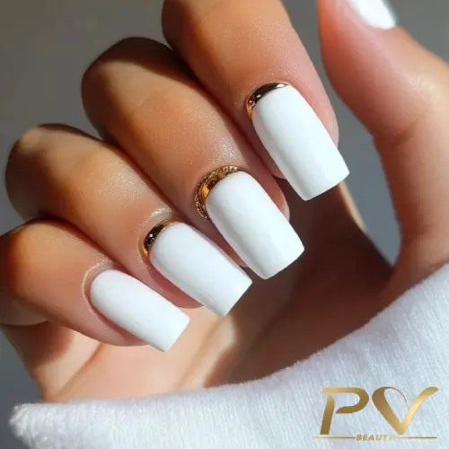 unhas-decoradas-branco-detalhes-dourados-pv-beauty-03 Unhas com esmalte branco e detalhes dourados perto das cutículas, em uma mão feminina.