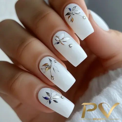 unhas-decoradas-branco-flores-modernas-pv-beauty-13 Unhas brancas decoradas com detalhes florais e pedrarias delicadas, exibindo um design sofisticado e elegante.