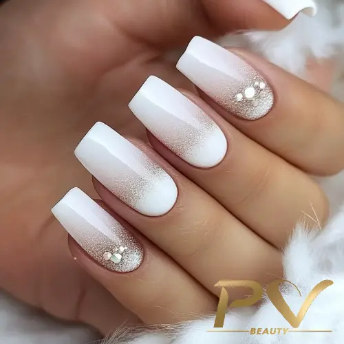 unhas-decoradas-branco-po-de-brilho-pv-beauty-07 Unhas quadradas com esmalte branco e decoração de strass em um fundo claro e macio.
