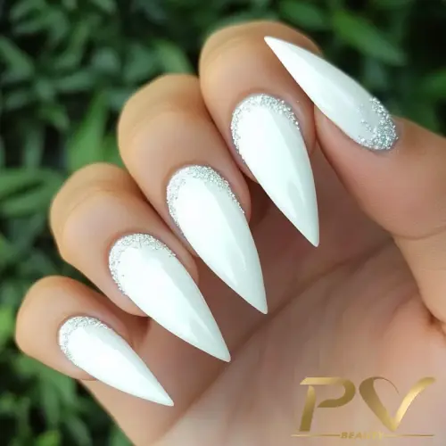unhas-decoradas-branco-stiletto-pv-beauty-04 Unhas alongadas e pontiagudas com esmalte branco e detalhes prateados nas cutículas, em fundo verde.