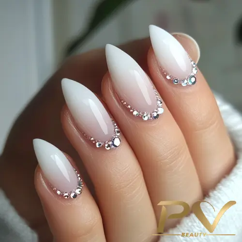 unhas-decoradas-branco-strass-lindos-pv-beauty-30 Unhas em formato stiletto com esmalte branco, decoradas com pequenas pedras brilhantes na base.