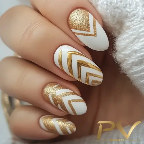 Unhas decoradas com esmalte branco e dourado, apresentando padrão geométrico e textura brilhante.