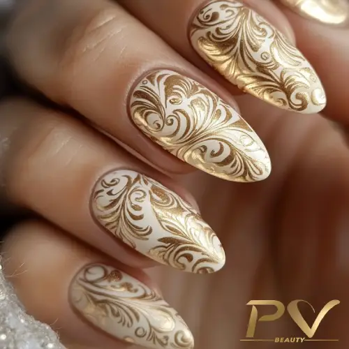 Unhas decoradas com desenhos elegantes em dourado sobre base clara.