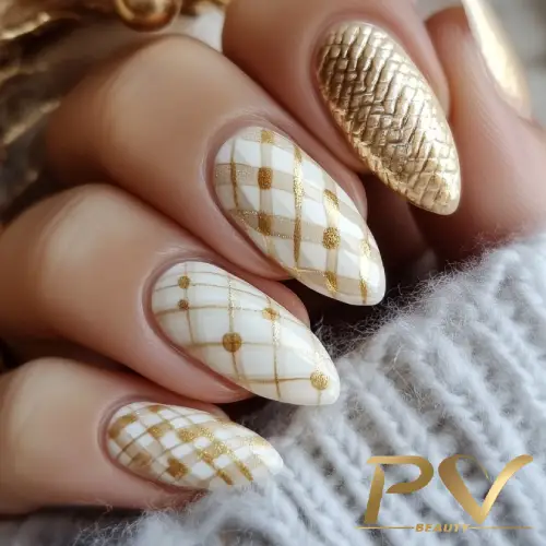 Unhas decoradas com esmalte dourado e branco, exibindo padrões geométricos e textura brilhante.