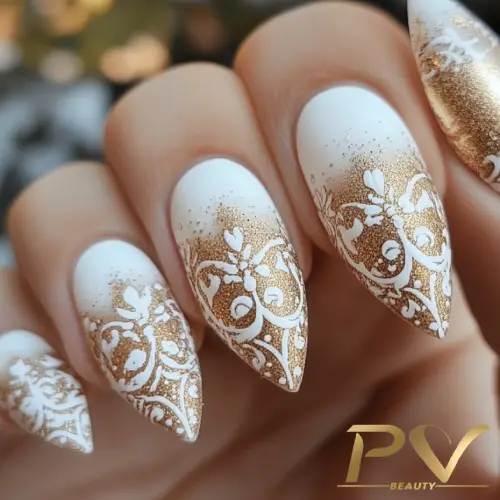 Unhas decoradas em formato stiletto com design branco e dourado detalhado.