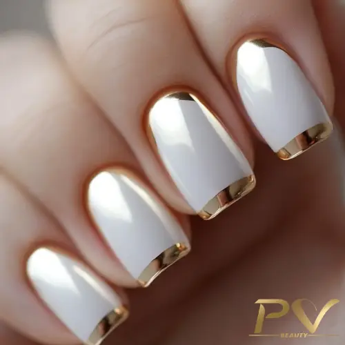 Unhas com esmalte branco e detalhes dourados nas pontas.