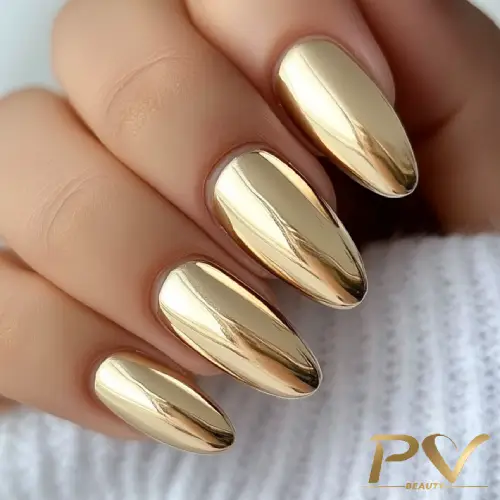 Unhas com esmalte metálico dourado, destacando-se sobre um fundo claro e texturizado.