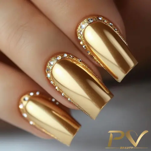 Unhas douradas com acabamento metálico e detalhes de pedras brilhantes ao redor das cutículas.