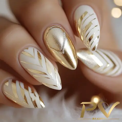 Unhas decoradas com esmalte dourado e branco, exibindo padrões geométricos e linhas metálicas.