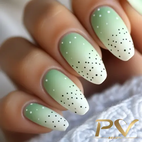 unhas-em-verde-decoradas-poa-pv-beauty-15 Unhas com esmalte verde ombré e pontilhado preto, segurando tecido branco.
