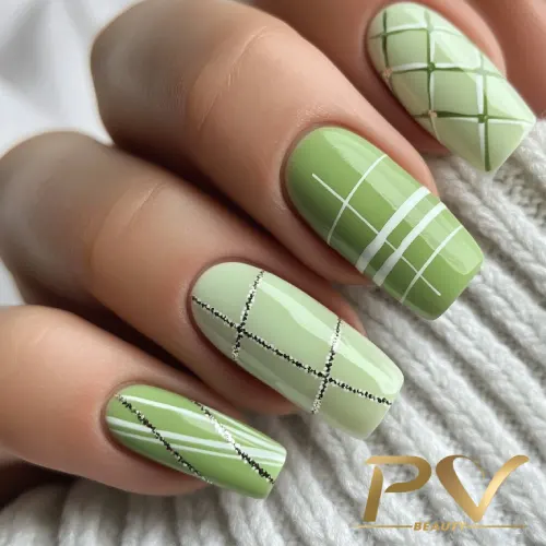 unhas-em-verde-decoradas-quadriculadas-pv-beauty-19 Unhas pintadas em tons de verde com padrões geométricos, incluindo linhas brancas e pretas, sobre tecido claro.