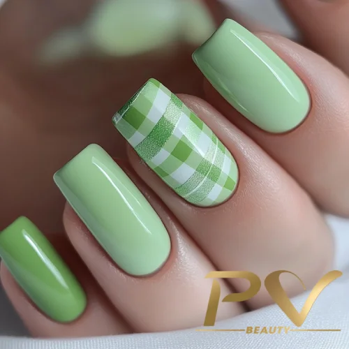 unhas-em-verde-decoradas-xadrez-pv-beauty-24 Unhas pintadas de verde claro com um padrão xadrez em verde e branco em um dedo.
