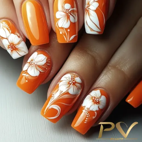 unhas-laranja-decoradas-quadradas-florais-pv-beauty-29 Unhas laranja com desenhos de flores brancas detalhadas, sobre uma superfície clara.