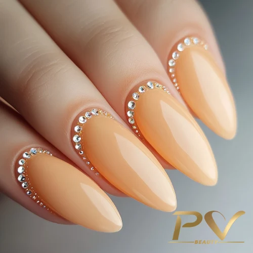 unhas-laranja-decoradas-suave-strass-pv-beauty-10 Unhas longas e pontiagudas com esmalte nude e detalhes de pedrinhas brilhantes ao redor das cutículas.