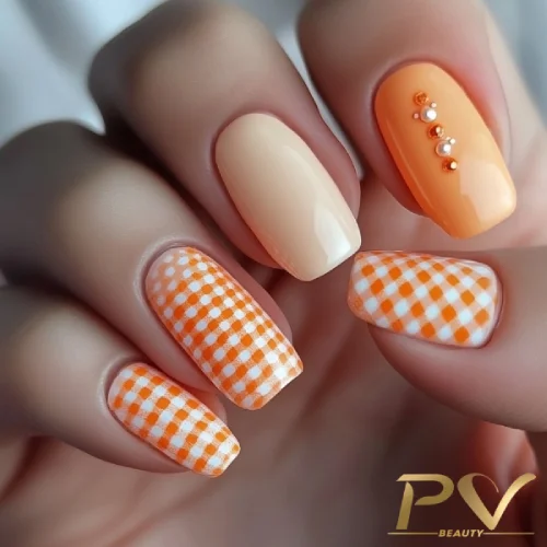 unhas-laranja-decoradas-xadrez-vichy-pv-beauty-08 Unhas decoradas com esmalte laranja e creme, incluindo padrão xadrez e detalhes com pequenas pedras.
