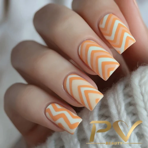 unhas-laranja-decoradas-zig-zag-pv-beauty-31 Unhas com esmalte laranja e branco em padrão de zig-zag, sobre tecido claro.