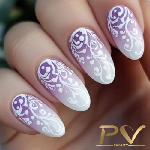 Unhas decoradas com esmalte degradê lilás e desenhos florais brancos detalhados.