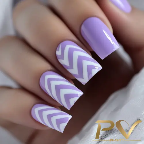 Unhas decoradas com esmalte lilás e branco, com padrão de zigue-zague em algumas unhas.