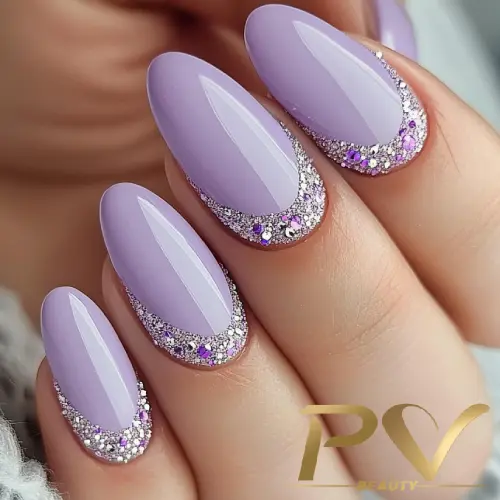 Unhas com esmalte lilás brilhante e detalhes prateados com glitter nas bordas, exibidas sobre um fundo neutro.