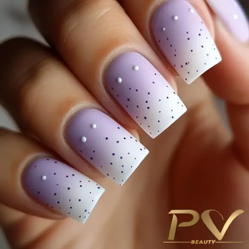 Unhas pintadas em tons de lilás e branco, decoradas com pontos pretos e pequenos detalhes brancos.