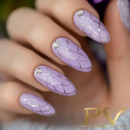 Unhas decoradas em tom lilás com padrão de linhas cruzadas e pequenas pedras brilhantes como detalhe.
