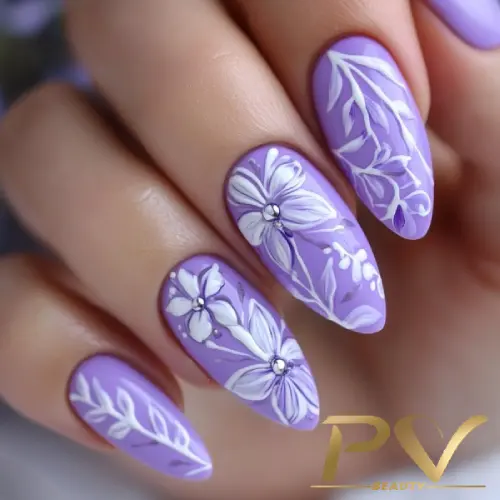 Unhas decoradas com esmalte lilás e desenhos florais brancos.
