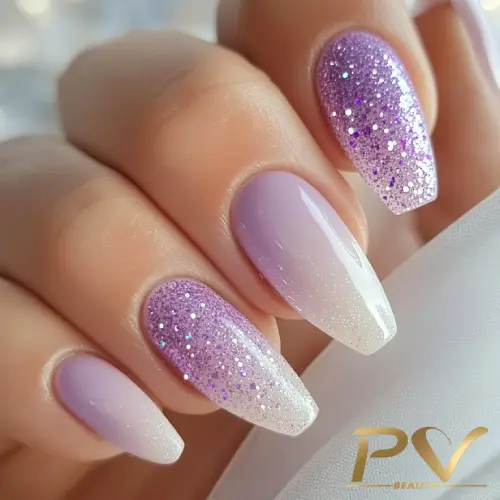 Unhas decoradas em tons de lilás, com brilho e efeito ombré, sobre fundo claro.