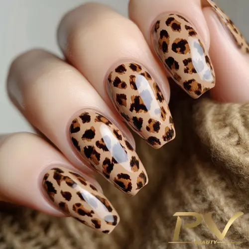 unhas-marrons-animal-print-oncinha-decoradas-pv-beauty-18 Unhas com esmalte estampado de oncinha, em tons de marrom e bege, sobre uma mão com fundo desfocado.