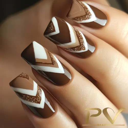 unhas-marrons-chevron-decoradas-pv-beauty-28 Unhas decoradas com esmalte marrom e branco, exibindo padrões geométricos em ziguezague.