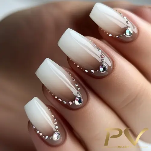 unhas-marrons-decoradas-pedrarias-pv-beauty-04 Unhas com esmalte em degradê branco e decoração de pedras prateadas brilhantes nas pontas.