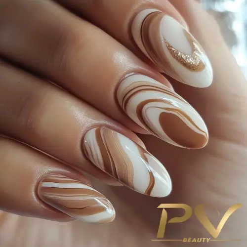 unhas-marrons-marmorizadas-decoradas-pv-beauty-11 Unhas decoradas com esmalte em tons de marrom e branco, com detalhes em dourado, formando um padrão marmorizado.