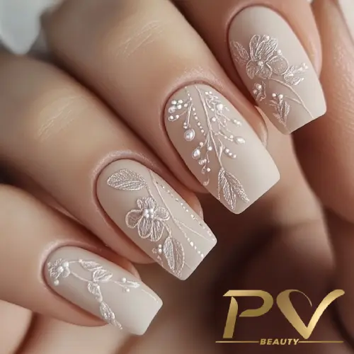 unhas-nude-foscas-florais-decoradas-pv-beauty-18 Unhas decoradas com esmalte nude e desenhos florais brancos em relevo, com detalhes de pérolas.