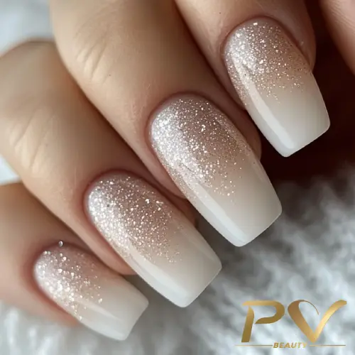 unhas-nude-glitter-ombre-decoradas-pv-beauty-08 Unhas com esmalte branco degradê e glitter, em close-up.