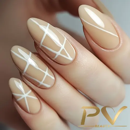 unhas-nude-linhas-assimetricas-decoradas-pv-beauty-19 Unhas decoradas com esmalte nude e linhas brancas cruzadas em design geométrico.