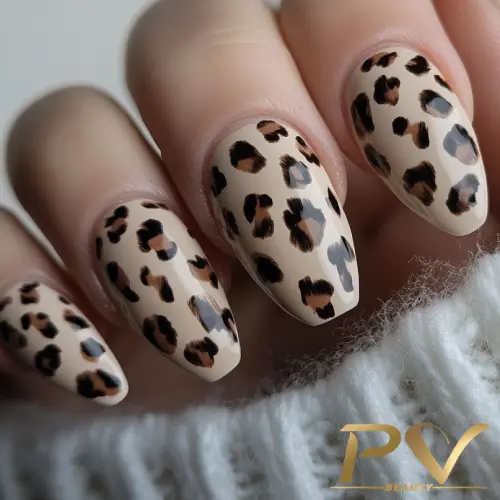 unhas-nude-oncinha-animal-print-fashion-decoradas-pv-beauty-12 Unhas decoradas com estampa de oncinha em tons de marrom e bege, próximas a um tecido cinza claro.