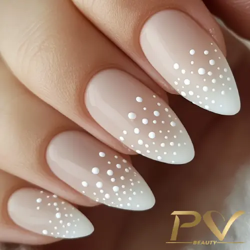 unhas-nude-poa-decoradas-pv-beauty-10 Unhas com esmalte nude e decoração de bolinhas brancas, em formato pontiagudo.