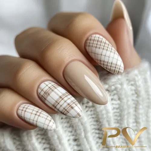 unhas-nude-xadrez-quadriculadas-decoradas-esmaltacao-pv-beauty-31 Mão com unhas longas e decoradas. Duas unhas têm estampa xadrez, enquanto as outras são bege lisas. Suéter cinza ao fundo.