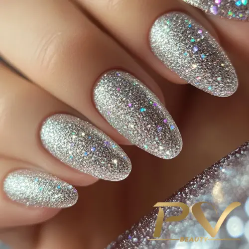 unhas-prata-glitter-decoradas-pv-beauty-33 Unhas decoradas com esmalte prateado brilhante e glitter, destacando-se em um fundo neutro.