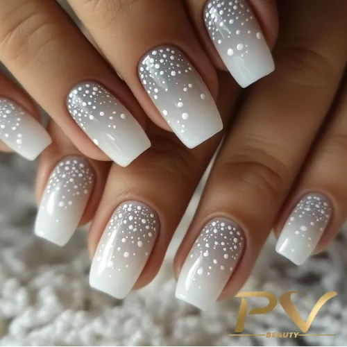 unhas-prata-poa-decoradas-pv-beauty-26 Unhas com esmalte ombré branco e cinza, decoradas com pequenas bolinhas brancas, em fundo desfocado.
