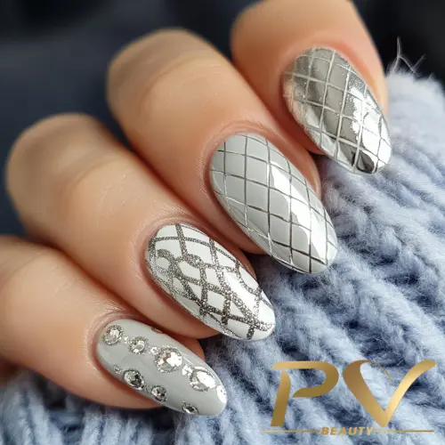 unhas-prata-quadriculadas-decoradas-pv-beauty-06 Unhas com esmalte prateado e desenhos geométricos, incluindo linhas cruzadas e aplicações brilhantes.