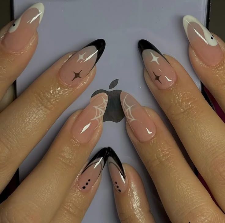 Unhas decoradas com desenhos de teias e estrelas em preto e branco sobre fundo rosa, segurando um dispositivo eletrônico.
