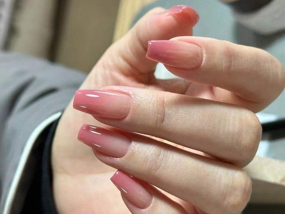 Mão com unhas longas e esmaltadas em tom rosa brilhante, mostrando detalhes do acabamento.