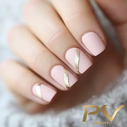 Unhas com esmalte rosa claro e detalhes de faixas douradas diagonais.