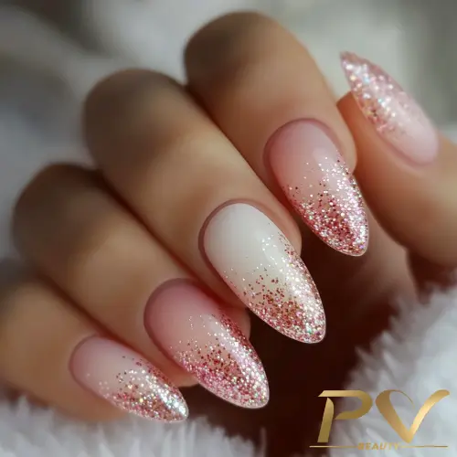 Unhas decoradas em formato stiletto com esmalte rosa e glitter brilhante nas pontas.